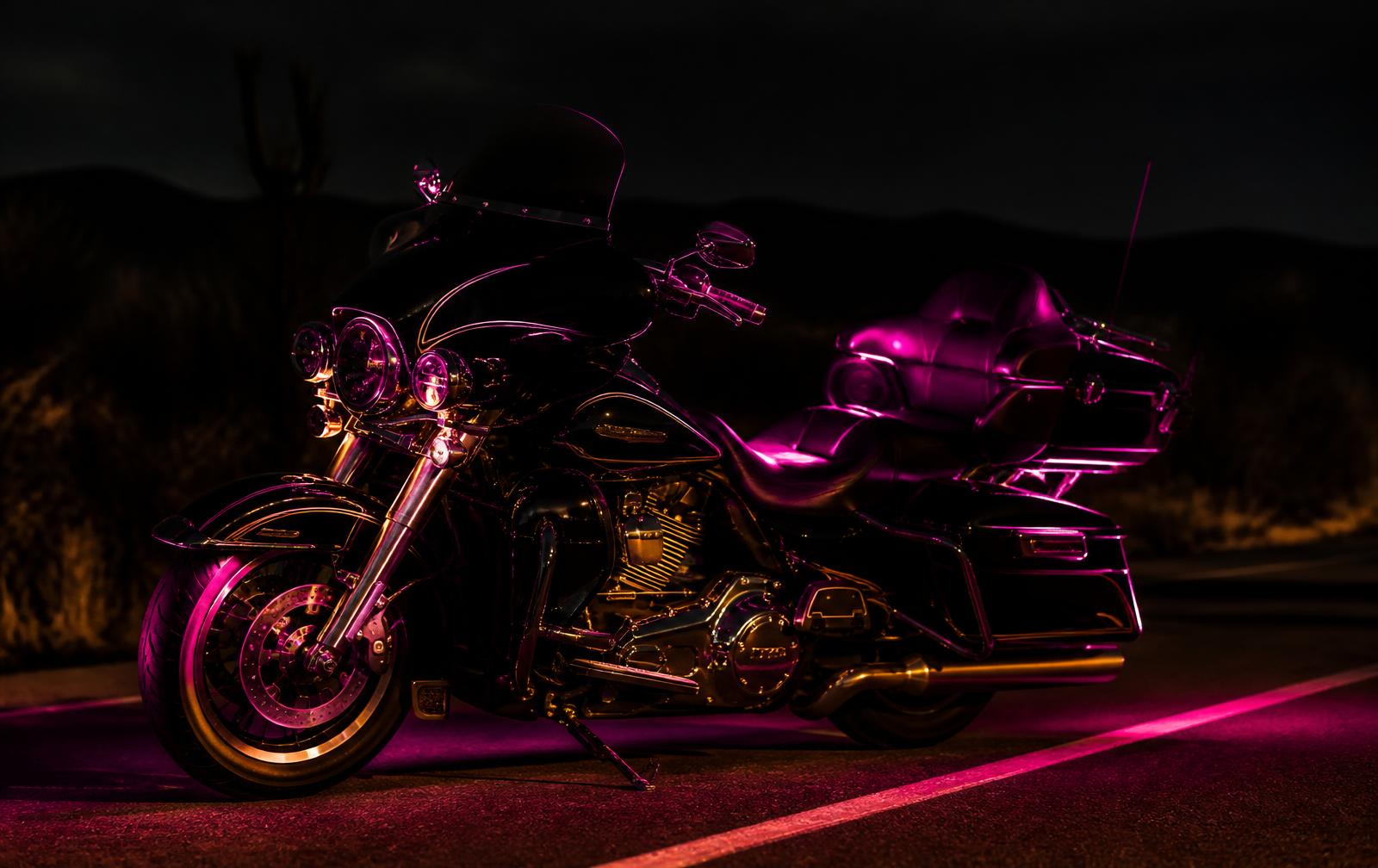 Gloss black touring motorcycle lit by magenta edge light on a night highway
